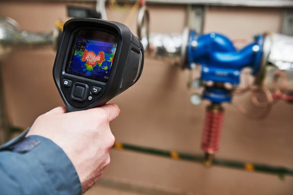 Inspector using a thermal camera on industrial equipment